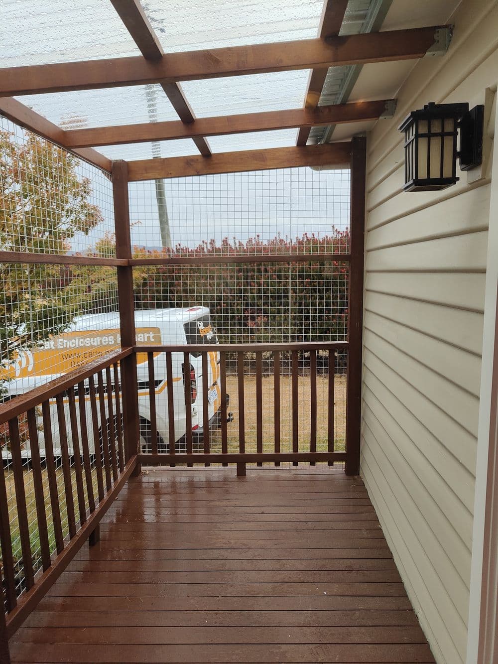 A verandah enclosed with timber framing, white mesh and a clear pergola roof